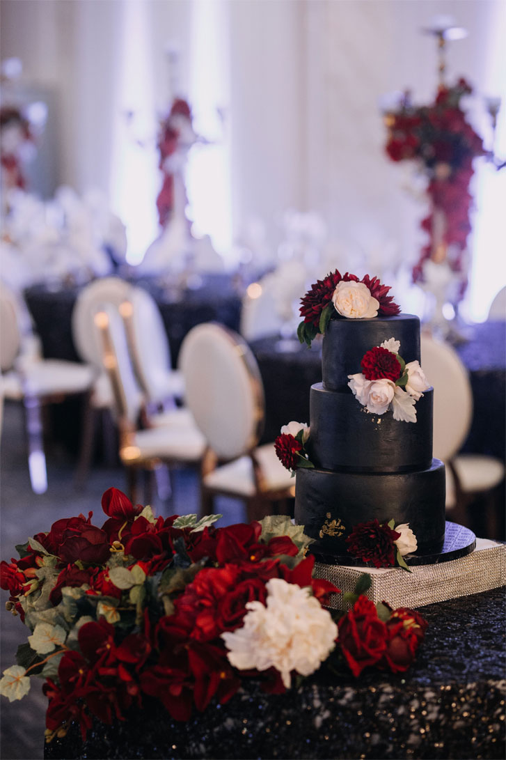 Three tier black wedding cake adorned with white and red flowers #weddingcake